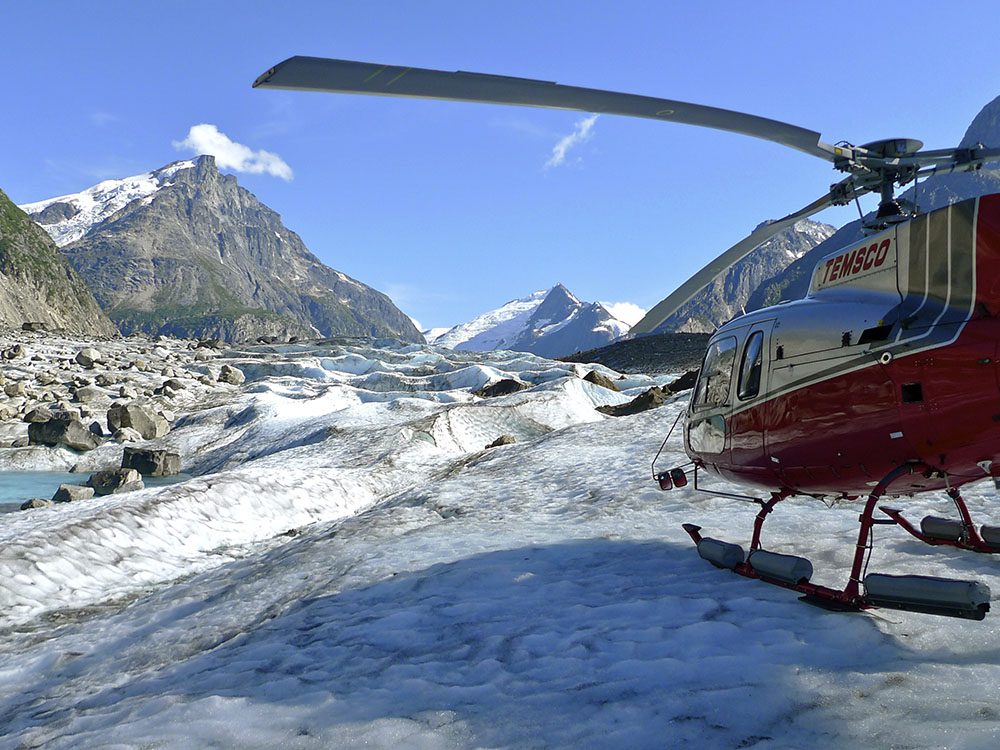 A helicopter is parked on the side of a snowy mountain.