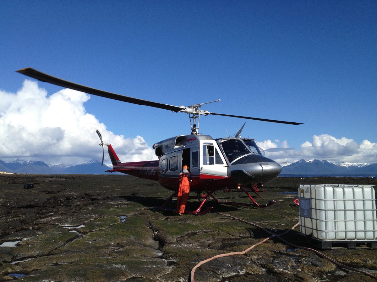 A helicopter is parked on the ground near some water tanks.