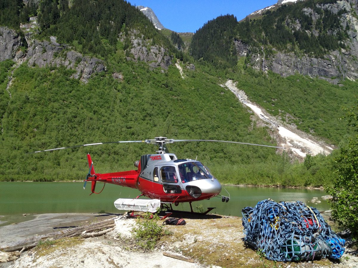 A helicopter is parked on the shore of a lake.