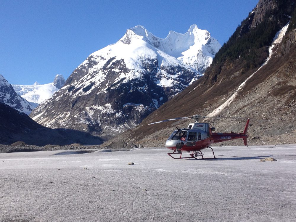 A helicopter is parked on the ground near some mountains.