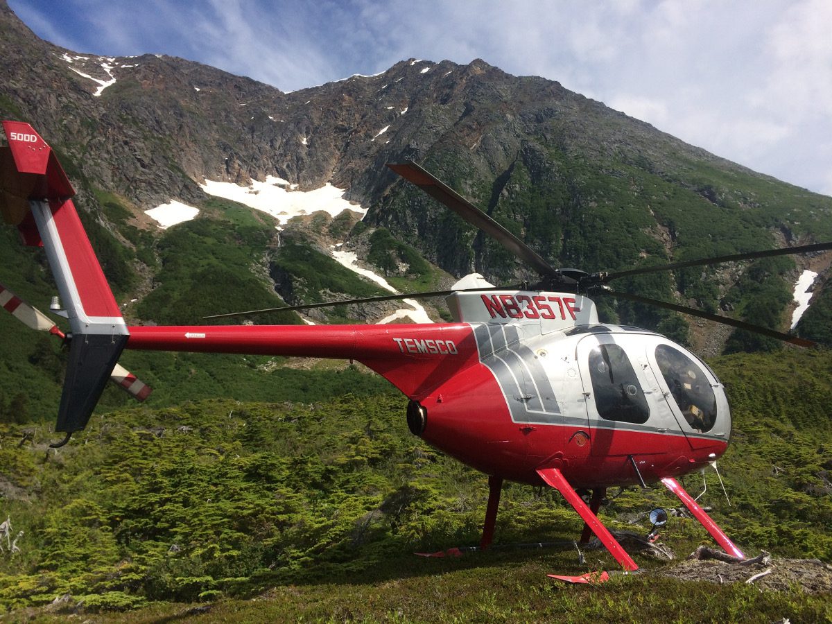 A red helicopter is parked on the side of a mountain.