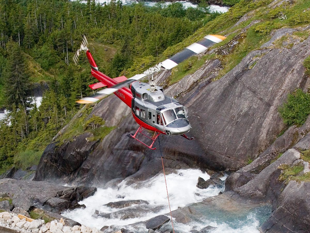 A helicopter flying over the side of a mountain.