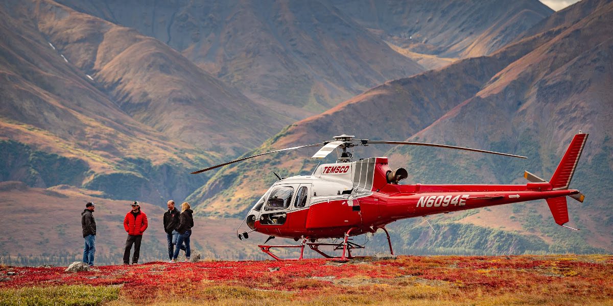 A helicopter is parked on the ground near two people.