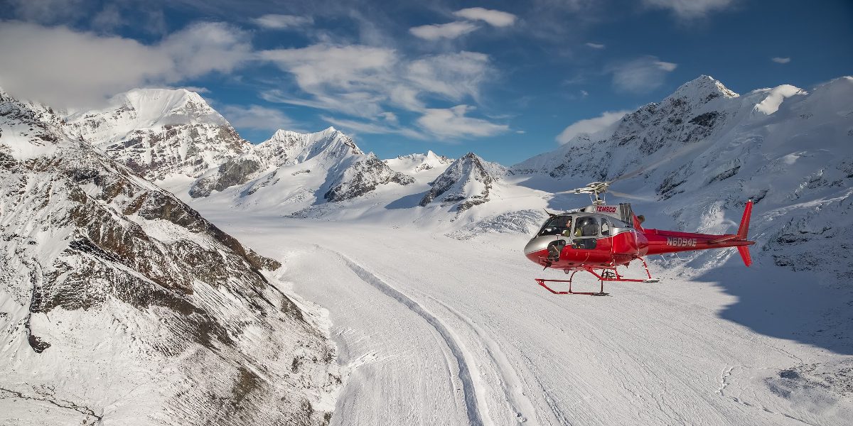 A helicopter is flying over the snow covered mountains.
