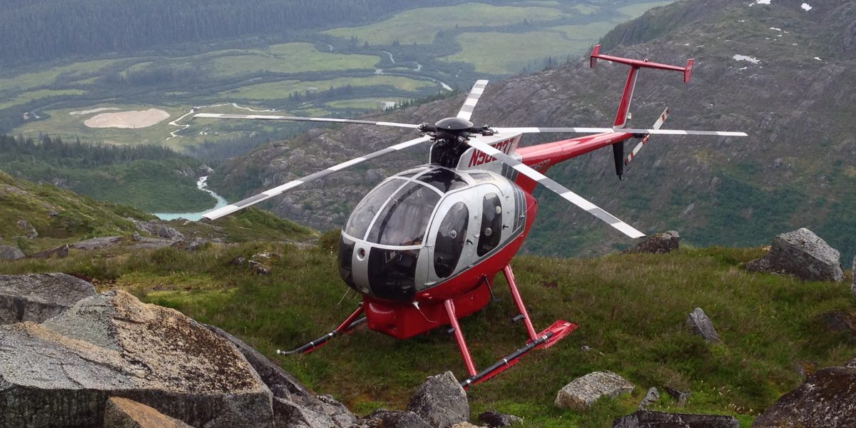 A helicopter is flying over the top of a mountain.