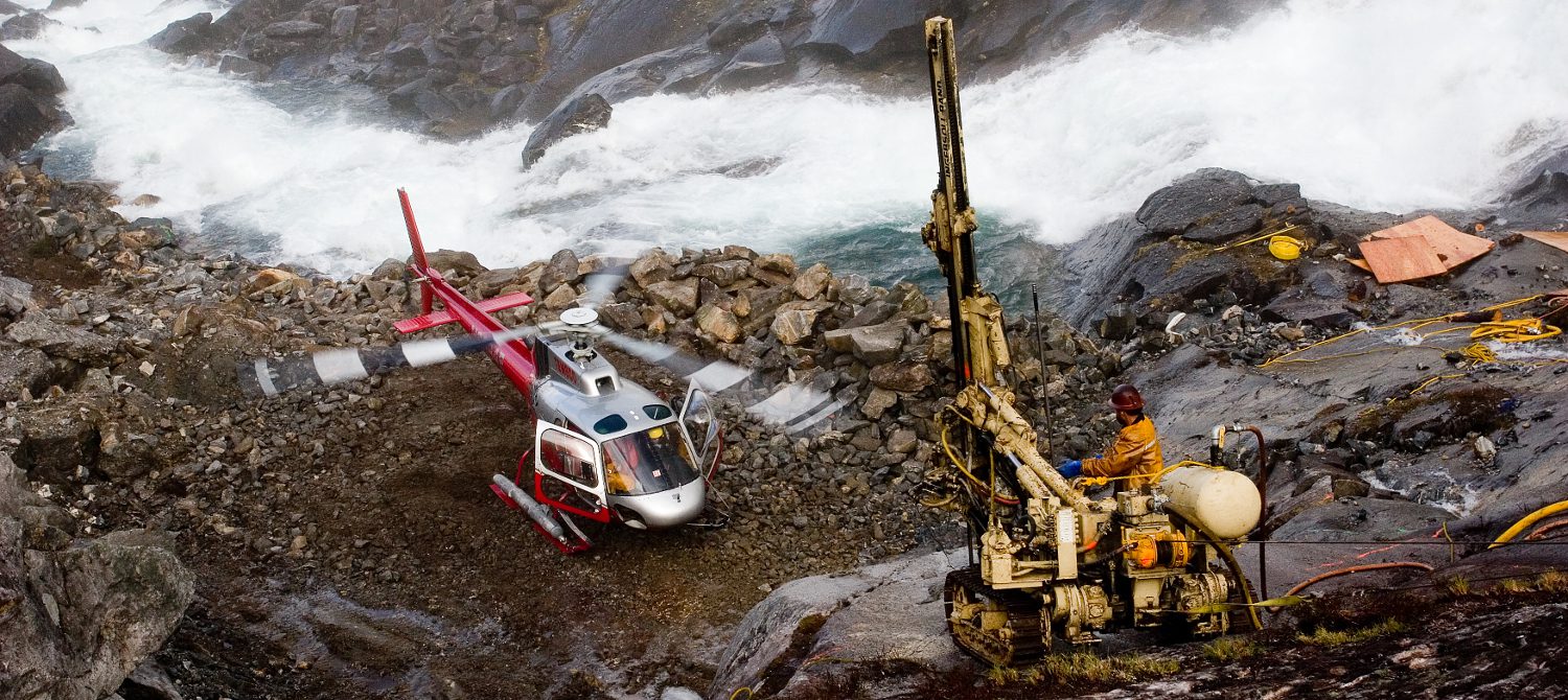 A helicopter is parked on the rocks near a crane.