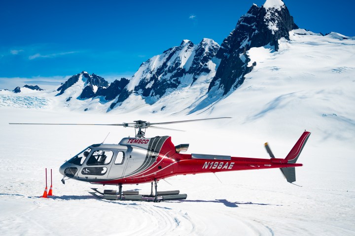 Red helicopter on snowy mountain landscape with a blue sky.
