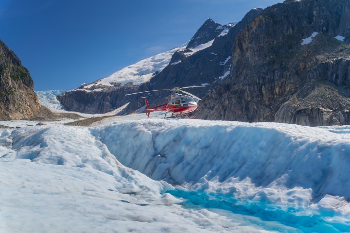 Red helicopter landed on a snowy glacier with rocky mountains in the background.